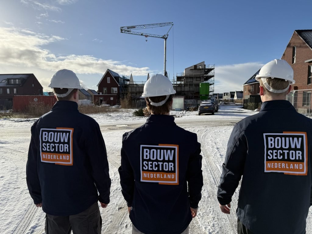 Teamleden in bedrijfskleding van Bouwsector Nederland kijken uit over besneeuwde nieuwbouwhuizen